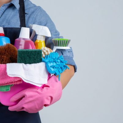 Young girl is holding cleaning product, gloves and rags in the basin on white background